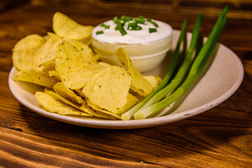 Ceramic plate with potato chips and glass bowl with sour cream on wooden table