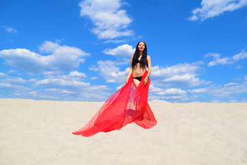 Naked brunette girl in a black swimsuit with a red towel on the sand. Hot summer.