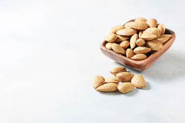 Raw almond in the sinks in a wooden bowl on a white background, selective focus. The concept of healthy food.