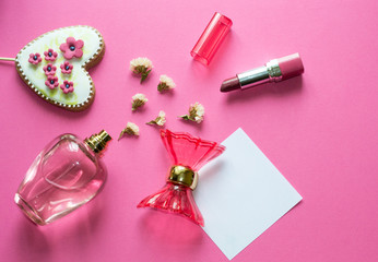 Love concept - pink adorable perfume, gingerbread heart, lipstick, flowers on pink background. Copy space for text. Woman make up tools.