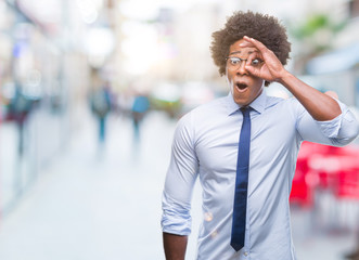 Fototapeta premium Afro american business man wearing glasses over isolated background doing ok gesture shocked with surprised face, eye looking through fingers. Unbelieving expression.
