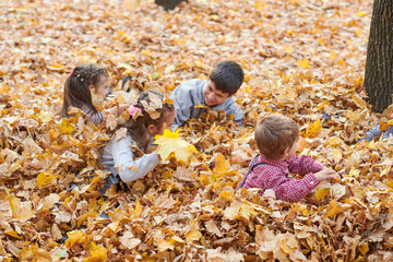 Children are lying and playing on fallen leaves in autumn city park.