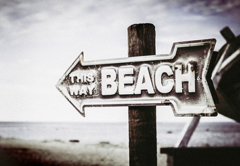Vintage artistic color arrow shaped sign showing way to the beach, on the pole on the beach, sea background.
