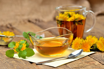 Dandelion honey, herbal tea, spoon, fresh mint leaves and dandelion head around