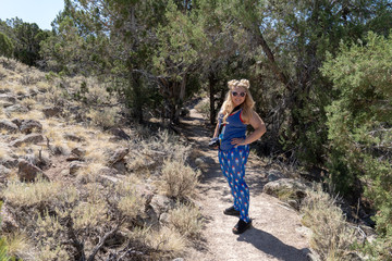 Naklejka premium Young blond woman hiker wearing goofy American patriotic clothing and sunglasses on a dirt trail at the ghost town of Old Irontown, Utah