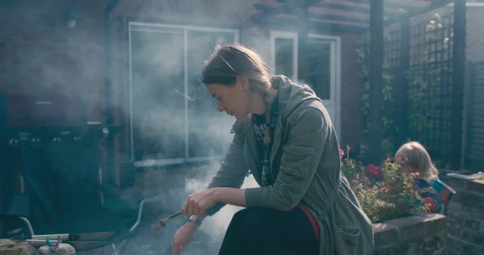 Young woman and toddler cooking food on smoking barbecue