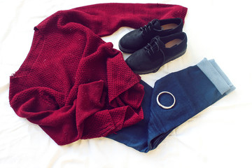 Naklejka premium blue jeans, red oversize knitted sweater and black flat shoes, bracelet on white sheet. Overhead view of woman's casual day outfits. Trendy hipster look.