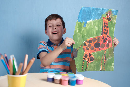 Happy Smiling European boy demonstrating picture he has painted at home.