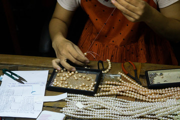 Close hand jeweler stringing pearls on a necklace. Worker in the production of Pearl Necklace