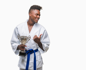 Young african american man over isolated background wearing kimono holding trophy pointing and showing with thumb up to the side with happy face smiling