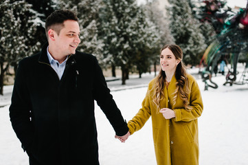 Young couple in love holding hands outdoor. Man and woman walk on a snowy winter park in love and leisure concept.