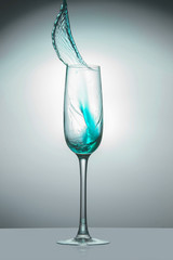 Transparent glass with light blue liquid jet up, close-up