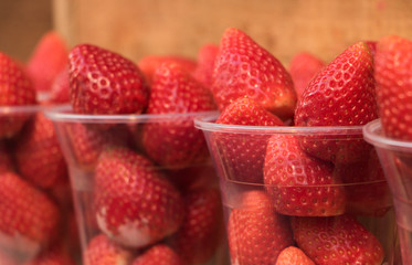 Close-up: delicious fresh strawberries are in disposable cups on a wooden shelf for sale. Concept: shopping & healthy tasty food.