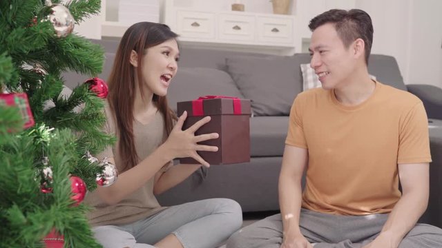 Asian couple man giving christmas gifts to his girlfriend in their living room at home in Christmas Festival. Lifestyle woman and man happy celebrate summer christmas and New year concept.