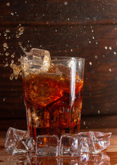 Glass still life image Cola with ice in a glass on a black wooden background