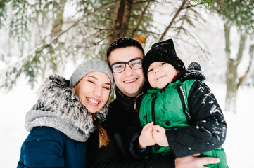 Portrait of happy family walking in a snow winter park. Father, mother and children boy are having fun and playing on snowy winter walk in nature.