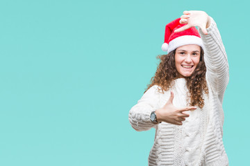 Young brunette girl wearing christmas hat over isolated background smiling making frame with hands and fingers with happy face. Creativity and photography concept.