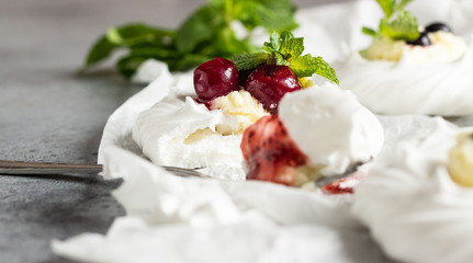 Mini Pavlova or meringue nests with whipped cream, berries and mint, selective focus. Grey concrete background. Copy space.