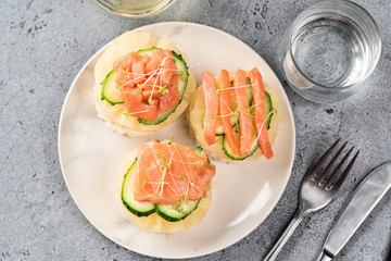 Bruschetta toast of white bread with slices of pineapple cucumber fish salmon and fresh green sprouts. Served on white plate table with mineral water, olive oil and fork with knife. Top view flat lay