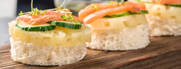 Bruschetta toast of white bread with slices of pineapple cucumber fish salmon and fresh green sprouts. Served on wooden serving board table with apple juice, wine, olive oil