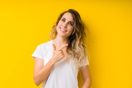Young beautiful blonde woman over yellow background cheerful with a smile of face pointing with hand and finger up to the side with happy and natural expression on face