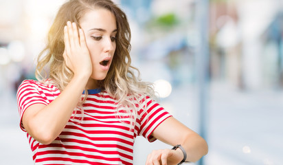 Beautiful young blonde woman over isolated background Looking at the watch time worried, afraid of...