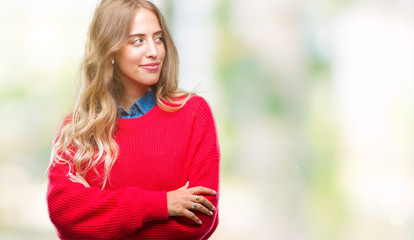 Beautiful young blonde woman wearing winter sweater over isolated background smiling looking side and staring away thinking.