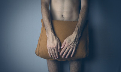 A young naked man covers his penis with a pillow.