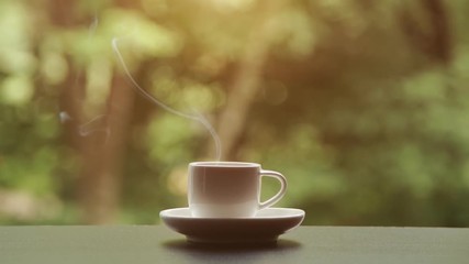 Hot steaming coffee or tea cup in the morning table and green nature background.