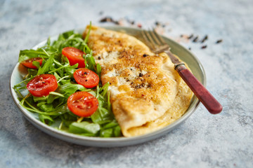 Classic egg omelette served with cherry tomato and arugula salad on side. Placed on white ceramic...