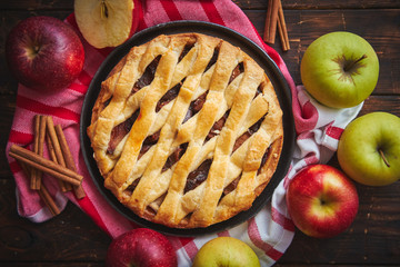 Traditional american apple pie served with fresh fruits, cinnamon sticks in a black ceramic plate. Flat lay and top view on rusty wooden table.