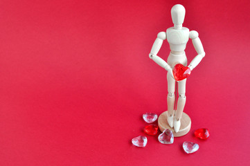 Bright concept for Valentine's day. Wooden model of a man holding a red heart on a red background.