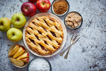 Delicious apple pie cake with a fresh red and green apples fruits, brown and powder sugar. Placed on rusty scratched stone table.