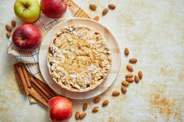 Freshly baked homemade apple pie with almond flakes cake on yellow rusty background. Fresh apple fruits, cinnamon sticks and icing sugar. Top view with copy space.