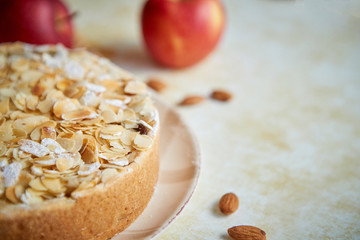 Freshly baked homemade apple pie with almond flakes cake on yellow rusty background. Fresh apple fruits, cinnamon sticks and icing sugar. Top view with copy space.