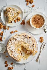 Vertical shot of a whole round delicious apple cake tart with almond flakes served on wooden table. With coffee in a cup and slice of a pie on soucer.