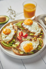 Delicious healthy breakfast with sliced avocado sandwiches with fried egg on top of bread. With orange juice, cherry tomatoes, radish sprouts, salt and peper. Flat lay, top view.