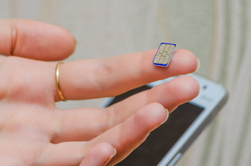 A girl holds the forefinger blue Nano SIM, smartphone in the background