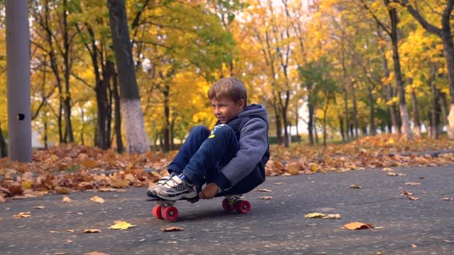 Young boy sitting and rolling on skateboard