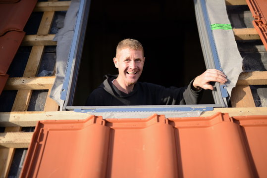 Dachdecker Beruf macht mit Erfolg Spa&szlig;, freundlicher Dachdecker Handwerker bei der Arbeit auf dem Dach am "Velux" Fenster