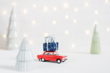 Red toy car with a christmas presents on the roof, garland bokeh on the background