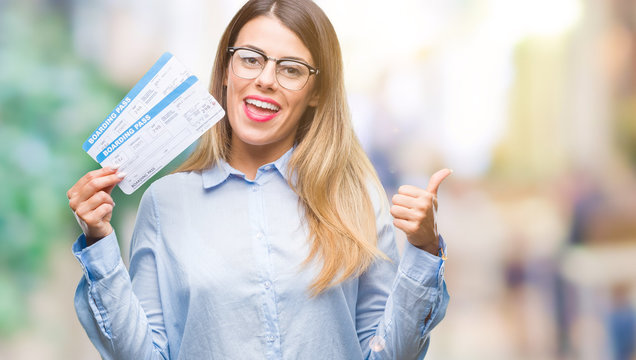 Young beautiful woman holding boarding pass over isolated background pointing and showing with thumb up to the side with happy face smiling