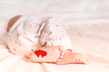 Baby foots with hearts on their feet. A newborn baby is lying on the bed.