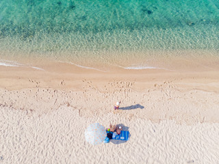 Fototapeta na wymiar Drone aerial view from above of sandy beach, sea water and three-member family on towel next to sunshade