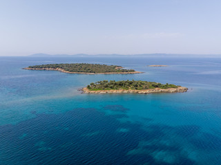 Two small islands surrounded with blue sea water with mountains in background. Drone aerial view