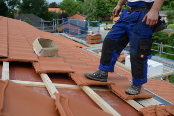 Dachdecker deckt rote Tonziegel mit Sturmklammern als Windsog Sicherung ein