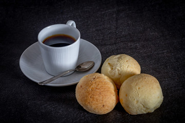 Brazilian homemade cheese bread, AKA 'pao de queijo' in a rustic background and a cup od coffee