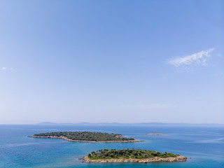 Two small islands surrounded with blue sea water with mountains in background. Drone aerial view