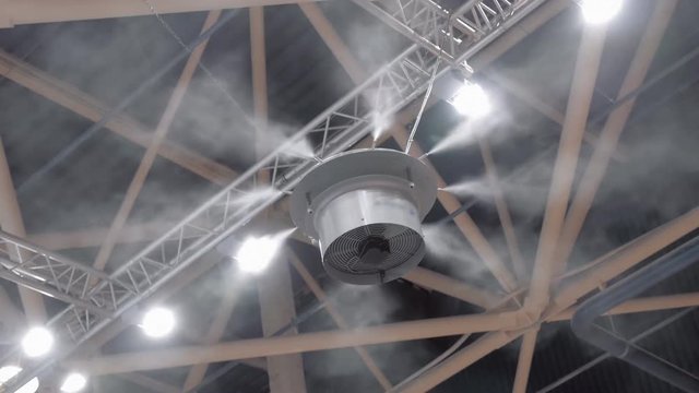 An industrial humidifier sprays water particles around itself at the ceiling of an industrial plant. Shot in motion
