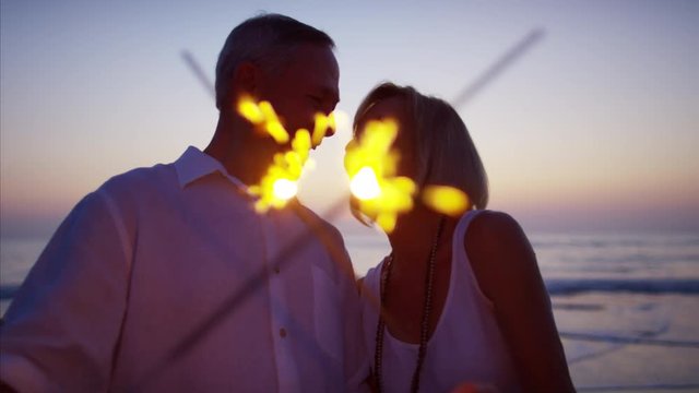 Retired Caucasian couple dancing with sparklers on the beach at sunset